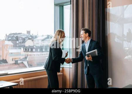 Uomini e donne professionisti felici che fanno stretta di mano in ufficio Foto Stock