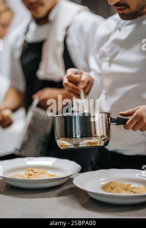 Chef maschile che tiene in mano una pentola mentre guardano il cibo in cucina al ristorante Foto Stock