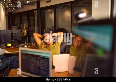 Programmatore donna sorridente che si rilassa con la mano dietro la testa in ufficio Foto Stock