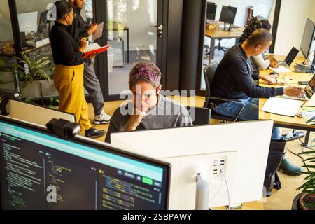 Visualizzazione ad angolo elevato del programmatore di computer non binari che lavora su un PC desktop in ufficio Foto Stock