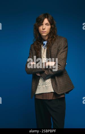 Un giovane uomo elegante si erge alto con le braccia incrociate, mostrando il suo abbigliamento alla moda e la sua fiducia. Foto Stock