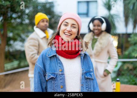 Giovane donna felice che indossa abiti invernali e sorride con due amici fuori fuoco dietro di lei Foto Stock