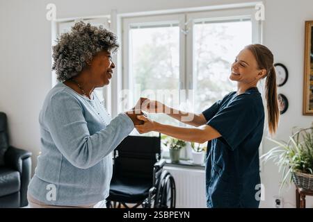 Felice medico donna che balla con una donna anziana a casa di riposo Foto Stock