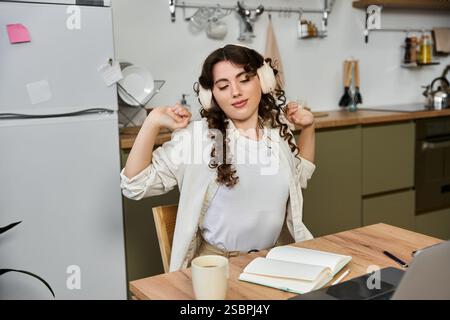 La giovane donna in una casa accogliente si allunga e si diverte con le sue canzoni preferite mentre sorseggia una bevanda calda. Foto Stock