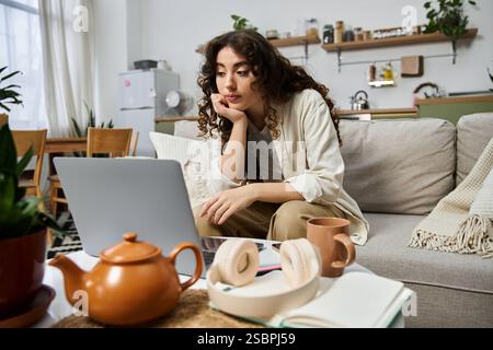 Una bella giovane donna è concentrata sul suo laptop, comodamente seduto nel suo elegante salotto. Foto Stock