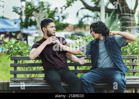 Due tizi che discutono seduti su una panchina. Due amici maschi che discutono su una panchina del parco Foto Stock
