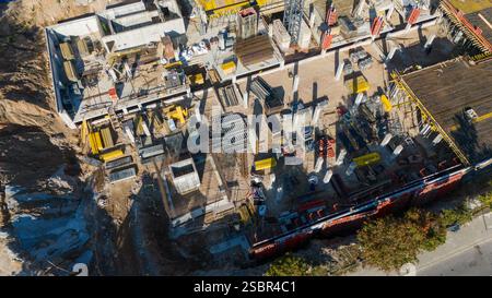 Vista aerea di un grande cantiere con vari macchinari e materiali da costruzione. Il sito è affollato da gru, ponteggi e operai Foto Stock