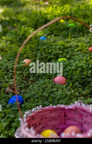 Le uova di Pasqua dai colori vivaci si diffondono su una vibrante erba verde, mentre nelle vicinanze si trova un cesto intrecciato, che indica una caccia all'uovo festosa in una vivace zona all'aperto Foto Stock