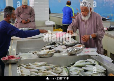 MUTTRAH, MASCATE, OMAN - 27 DICEMBRE 2024: Il mercato del pesce mattutino di Muttrah con venditori e clienti locali vestiti tradizionalmente Foto Stock