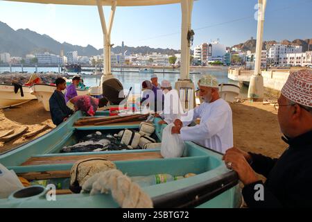 MUTTRAH, MASCATE, OMAN - 27 DICEMBRE 2024: Il porto dei pesci vicino al mercato del pesce con pescatori che vendono pesce dalla loro barca, con Muttrah corniche Foto Stock