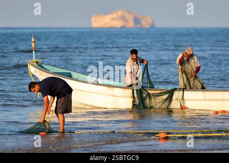 QURUM BEACH, MASCATE, OMAN - 28 DICEMBRE 2024: Pescatori dell'Oman che tornano dalla pesca e lavorano sulle reti da pesca sulla spiaggia di Qurum Foto Stock