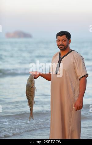 QURUM BEACH, MASCATE, OMAN - 28 DICEMBRE 2024: Ritratto di un pescatore omanita di ritorno dalla pesca e con in mano un pesce sulla spiaggia di Qurum Foto Stock