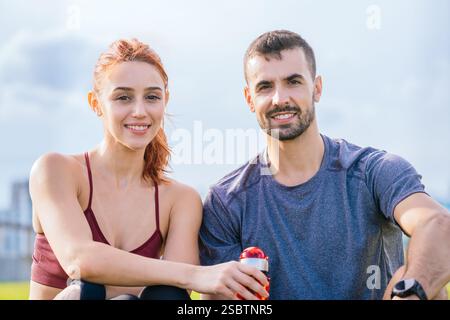 Coppia in forma sorridente che riposa all'aperto dopo l'allenamento con una bevanda rinfrescante Foto Stock