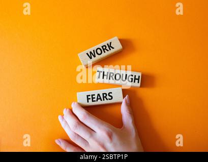 Lavorare attraverso il simbolo paure. I blocchi di legno con le parole passano attraverso le paure. Mano d'affari. Bellissimo sfondo arancione. Affari e lavoro attraverso le paure Foto Stock
