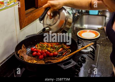 Bistecca con cipolle e pomodori rossi preparati in una cucina residenziale. Foto Stock