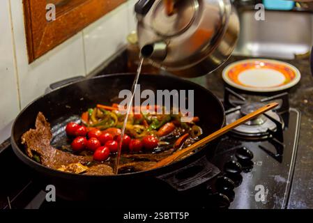 Bistecca con cipolle e pomodori rossi preparati in una cucina residenziale. Foto Stock