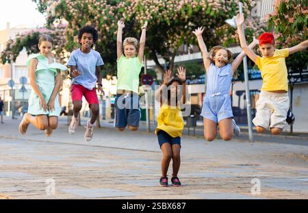 Allegre ragazze e ragazzi che saltano insieme sulla strada estiva della città Foto Stock