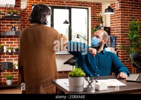 Colleghi caucasici che si salutano a vicenda in una stanza a muro di mattoni, pronti per la sessione di brainstorming. Un manager maschio seduto alla scrivania, scambiando dossi a gomito con una collega donna nell'ufficio delle startup. Foto Stock