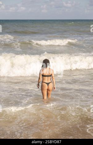 Donna di mezza età che cammina nell'oceano portata da dietro in costume da bagno al Grand Palladium Imbassai, Salvador de Bahia, Brasile Foto Stock