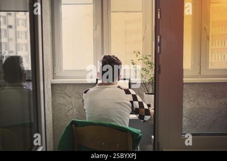 Vista posteriore di un uomo seduto a una scrivania che utilizza un laptop al tramonto Foto Stock