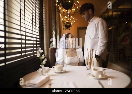 Gli sposi e gli sposi condividono un momento intimo in un caffè con luce soffusa Foto Stock
