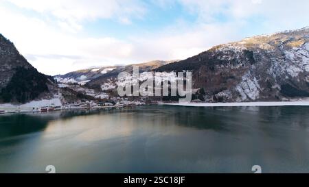 Vista aerea invernale di Gaupne, Norvegia, con un tranquillo fiordo che riflette le colline innevate, case sparse e un affascinante villaggio rurale nella valle panoramica. Foto Stock