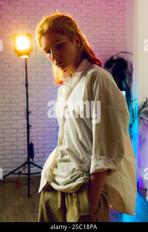 Un giovane in uno studio artistico con illuminazione colorata mette in mostra uno stile di moda moderno durante una sessione creativa Foto Stock