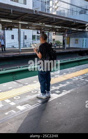 Hip Young Woman che legge sul binario dei treni alla stazione Nakano di Tokyo in Giappone Foto Stock