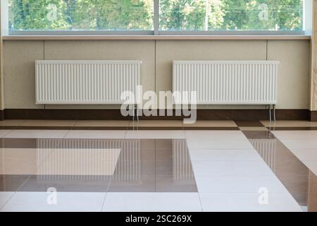 Due lunghi radiatori bianchi dell'impianto di riscaldamento installati sotto il finestrino. Foto Stock