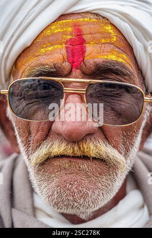 13 gennaio 2025, Prayagraj, uttar Pradesh, India. Primo piano di un vecchio che indossa occhiali da sole con un tilak di zafferano, trasudando saggezza. Foto Stock