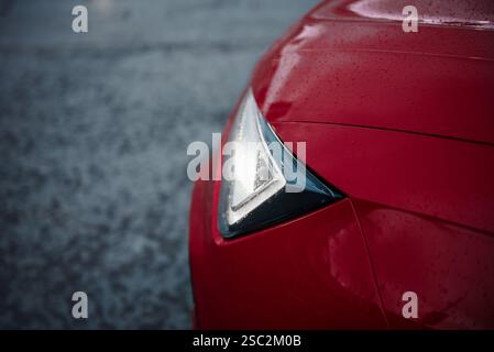 Auto moderna rossa con fari a LED luminosi - vista parafango anteriore. Superficie in cemento sfocata sullo sfondo. Foto Stock