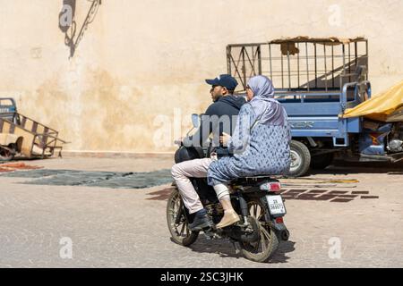 uomo e donna in abbigliamento tradizionale senza caschi in sella a una moto per la strada della medina. Marrakech, Marocco Foto Stock