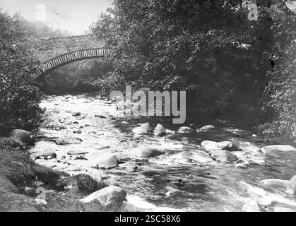 Una vista dalla strada di uno stretto ponte sul fiume sulla strada per le cascate Aber, note anche come Rhaeadr Fawr in gallese, situato vicino al villaggio di Abergwyngregyn, a circa tre miglia a sud di Trefriw. La cascata è formata dall'Afon Goch ai piedi della catena montuosa Carneddau nel Galles del Nord. 1900, monocromatico: Da un'importante collezione storica di fotografie di albumi originali, non attribuite, dal tardo Vittoriano al primo edoardiano: Un tour britannico che include Staffordshire, Warwickshire e Galles del Nord. La qualità degli originali era variabile e la maggior parte era di circa 10 Foto Stock