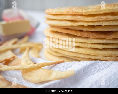Una pila di strati di burro rotondi e sottili al forno, frammenti di impasto e burro su un asciugamano bianco pronto per preparare una pasta sfoglia a pasta frolla Napoleone. Foto Stock