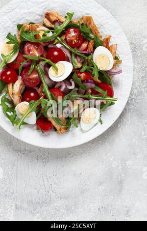 Un'insalata calda con filetto di pollo fritto, rucola e pomodori ciliegini, e uova di quaglia bollite, su un piatto bianco, non c'è gente Foto Stock