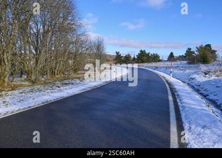 Una strada tortuosa conduce attraverso un paesaggio innevato con alberi e un cielo azzurro limpido, inverno, Oberelsbach, Lange Rhoen, Rhoen, Baviera, Germania, Euro Foto Stock