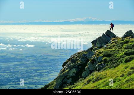 Alpinismo donna in piedi su rocce e guardando il mare di nebbia nelle pianure italiane, Alpi Cozie sullo sfondo, colonna di Mombarone, GTA, grande Foto Stock