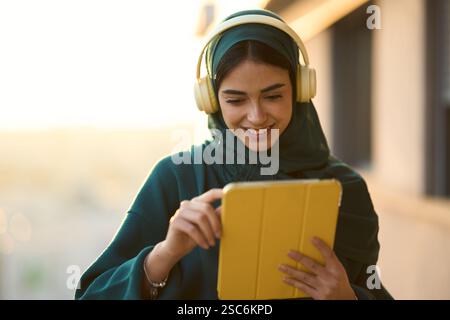Studente musulmano sorridente che ascolta la musica e usa il tablet al tramonto Foto Stock