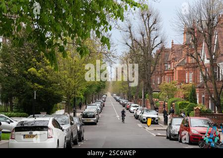 Ciclista su Winchester Road, NW3, Londra. Auto parcheggiate lungo la strada. Giorno di primavera. Foto Stock