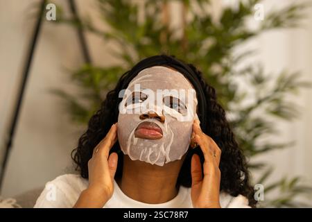 Giovane donna che applica una maschera viso cosmetica ringiovanente, assaporando un momento felice di cura di sé e relax nell'ambiente rilassante di lei Foto Stock
