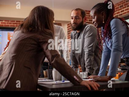 Primo piano di un team eterogeneo appoggiato al tavolo, profondamente impegnato nella discussione di importanti questioni aziendali. Collaborazione di gruppo con strumenti digitali e documenti finanziari nella sala riunioni a muro. Foto Stock