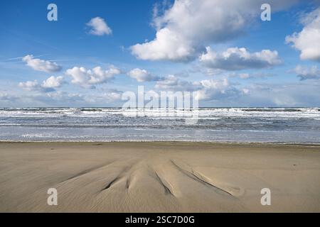 Una tranquilla spiaggia con onde dolci e un cielo nuvoloso. Foto Stock