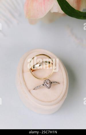 Due fedi nuziali splendidamente progettate poggiano su un delicato cuscino in tessuto, che simboleggia l'amore e la devozione. La fascia dorata completa l'intricata diamo Foto Stock
