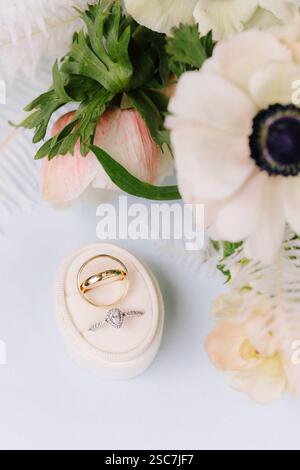 Due bellissime fedi nuziali riposano su un morbido cuscino, con una morbida disposizione floreale pastello nelle vicinanze, che crea un'atmosfera romantica e intima ideale per chi desidera sposarsi Foto Stock