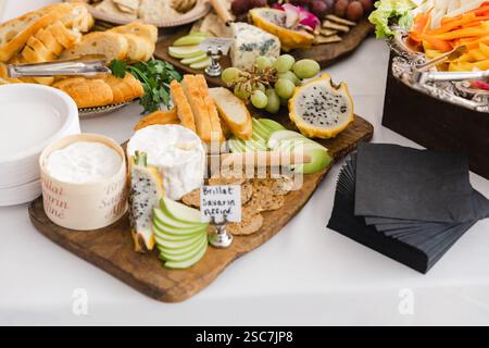 Un variopinto assortimento di formaggi, frutta e pane è splendidamente esposto su una tavola di legno in un vivace raduno. La presentazione invita gli ospiti Foto Stock