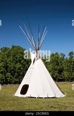 Un teepee sta in un campo. Il tepee è bianco e ha un tetto appuntito Foto Stock