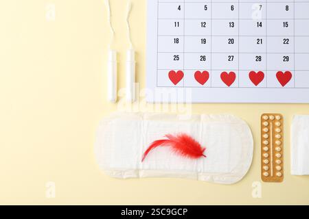 Composizione piatta con calendario e prodotti mestruali su sfondo beige Foto Stock
