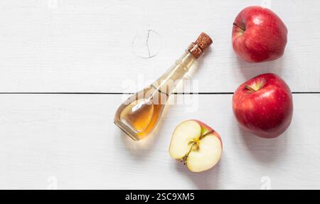 Bottiglia in vetro di aceto biologico di sidro di mele con mele rosse mature su fondo in legno, messa a fuoco selettiva, spazio per il testo Foto Stock