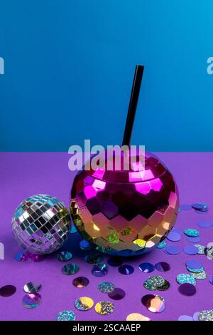 Una grande palla da discoteca rosa e una piccola palla da discoteca argentata poggiano su una colorata superficie viola disseminata di coriandoli lucenti, suggerendo un'atmosfera da festa. Foto Stock