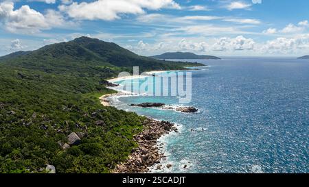 Le rocce di granito sparsi lungo la costa incontrano acque turchesi, delimitate da una vegetazione lussureggiante e da sabbie bianche. Seychelles, la Digue. Foto Stock